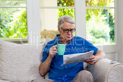 Senior man reading newspaper while having coffee at home