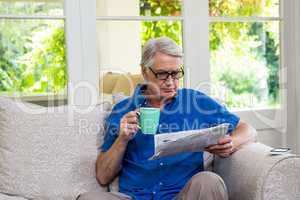 Senior man reading newspaper while having coffee at home