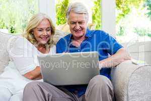 Exited senior couple using laptop while sitting in living room a