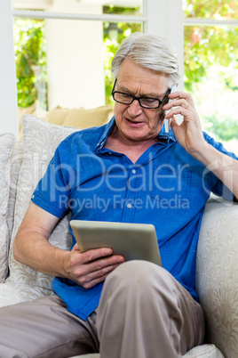 Senior man using mobile phone and digital tablet at home