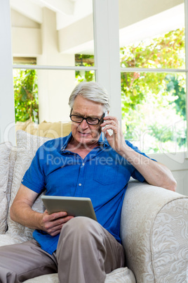 Senior man using mobile phone with digital tablet at home