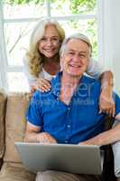 Happy senior couple with laptop sitting on sofa at home