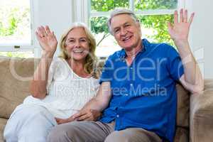 Happy senior couple waving hands while sitting at home