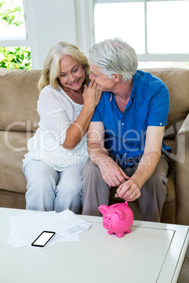 Senior couple putting coin in piggi bank while sitting at home