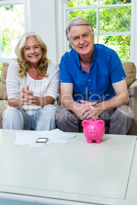 Happy senior couple sitting with piggi bank in living room at ho