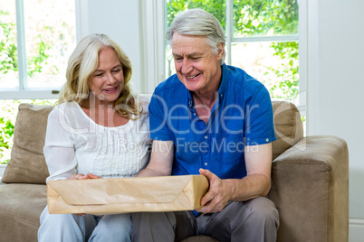 Senior couple holding parcel while sitting in living room at hom