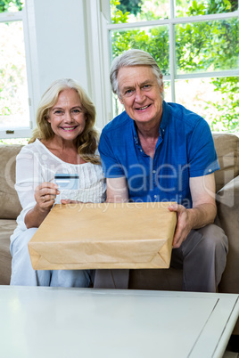 Happy senior couple holding parcel with smart card at home