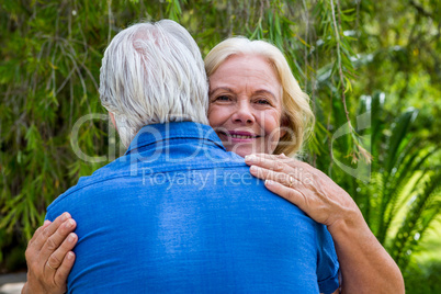 Senior woman hugging man against tree at park