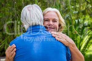 Senior woman hugging man against tree at park