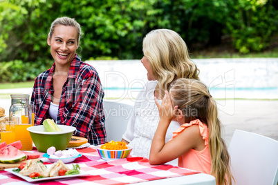 Smiling woman taking to mother and daughter at table Smiling woman taking to mother and daughter at table