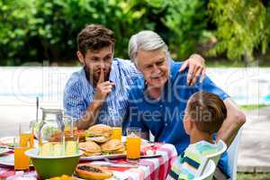 Man gesturing silence while son talking with grandfather at lawn