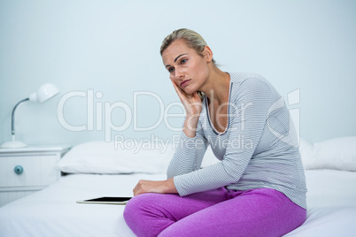 Thoughtful woman sitting by digital tablet on bed