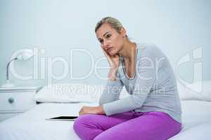 Thoughtful woman sitting by digital tablet on bed