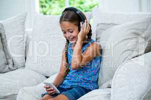 Girl holding phone while listening to music on sofa