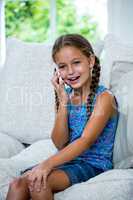 Happy girl talking on mobile phone while sitting on sofa