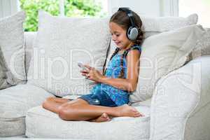 Girl using mobile phone while listening music on sofa