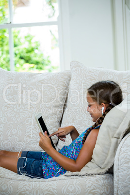 Girl using digital tablet while relaxing on sofa