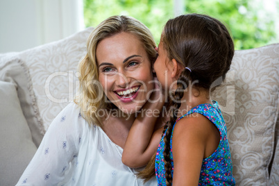 Girl whispering in smiling mother ear