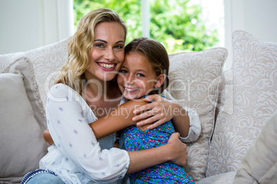 Portrait of mother and daughter embracing on sofa