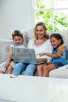 Happy children with mother using laptop on sofa