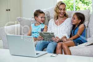 Mother sitting with daughter and son using tablet on sofa