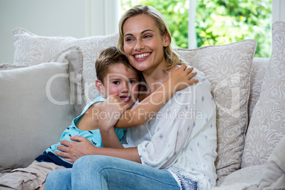 Cheerful son embracing mother on sofa