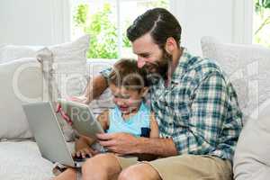 Playful son and father with laptop and digital tablet on sofa