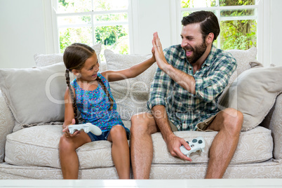 Father and daughter doing high five while sitting on sofa