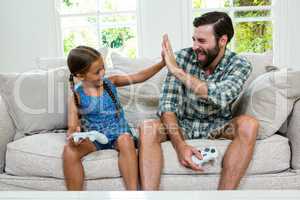 Father and daughter doing high five while sitting on sofa