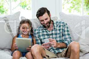 Playful daughter and father with digital tablet and mobile on so