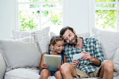 Father showing mobile phone to daughter while sitting on sofa