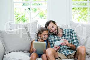 Father showing mobile phone to daughter while sitting on sofa