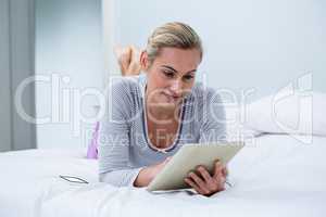 Young smiling woman using digital tablet while lying on bed