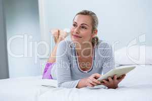 Smiling woman with digital tablet while lying on bed