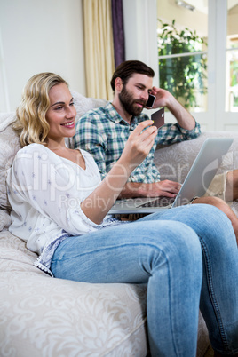 Woman holding credit card by man talking on phone with laptop