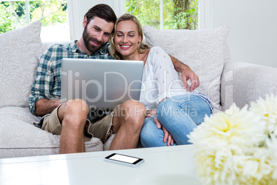 Happy young couple using laptop while sitting on sofa