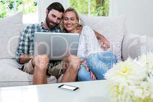 Happy young couple using laptop while sitting on sofa