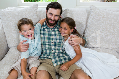 Cheerful father with son and daughter on sofa