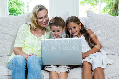 Happy mother by son and daughter using laptop at home