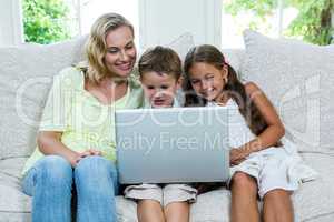 Happy mother by son and daughter using laptop at home