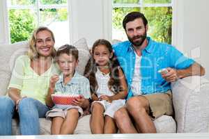 Portrait of family watching tv while sitting on sofa