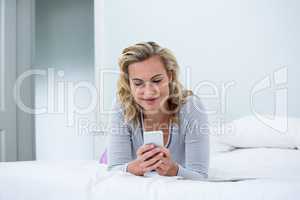 Smiling woman using phone while lying on bed