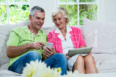 Husband showing mobile phone to senior woman on sofa