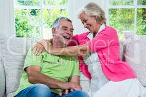 Romantic senior woman laughing with husband on sofa