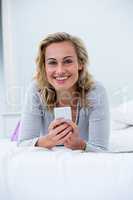 Young woman with mobile phone lying on bed