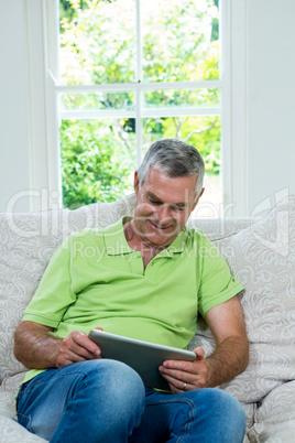 Happy senior man with digital tablet in sitting room