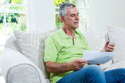 Senior man holding documents and mobile phone in sitting room