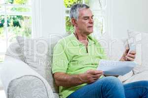 Senior man holding documents and mobile phone in sitting room
