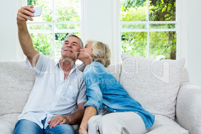 Senior woman kissing while man taking selfie in sitting room