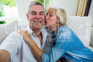 Excited senior woman kissing husband while sitting on sofa